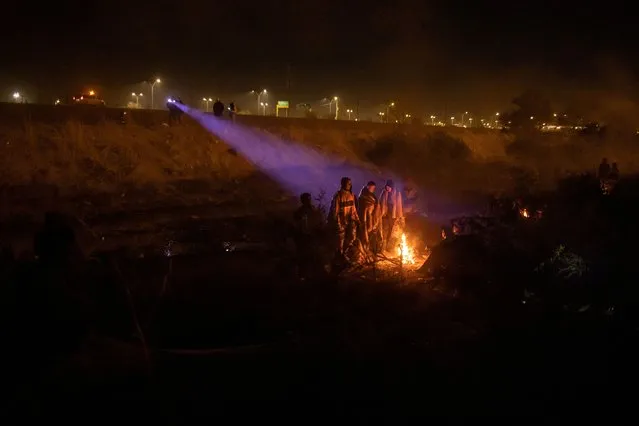 Officials with the National Institute of Migration (Instituto Nacional de Migracion) shine their flashlights from Ciudad Juarez, Mexico, towards migrants taking refuge along the dry riverbed of the Rio Grande as migrants gather around a fire while searching for an entry point into the United States, as seen from El Paso, Texas, on April 2, 2024. (Photo by Adrees Latif/Reuters)