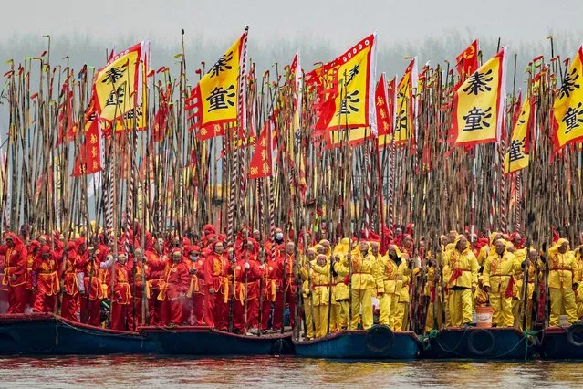 Participants stand with poles and flags on their traditional boats during the Taizhou Jiangyan Qintong Boat Festival at the Qinhu National Wetland Park in Taizhou, in eastern China's Jiangsu province on April 6, 2024. (Photo by AFP Photo/China Stringer Network)
