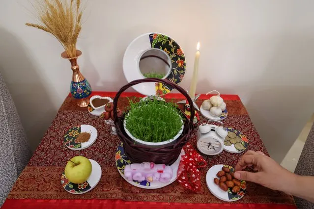 An Iranian decorates a table with "Haft Seen" or “Seven S” in Tehran on March 17, 2024, in preparation for Nowruz, the Persian New Year. Iranians celebrate Nowruz by decorating a floorcloth with seven items their names starting with the letter “S” in the Persian language; an apple (Seeb), garlic and vinegar (Seer-0-Serkeh), a coin (Sekkeh), sprouts (Sabzeh), sumac (Somagh), elaeagnus olives (Senjed) and the juice of germinating wheat or malt mixed with flour (Samanou), in addition to other propitious item like Islam's holy book the Koran, mirrors, flowers, goldfish, eggs and candles. (Photo by Atta Kenare/AFP Photo)