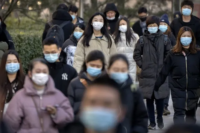 Commuters wearing face masks to help protect against the coronavirus walk along a street in the central business district in Beijing, Thursday, January 13, 2022. Just weeks before hosting the Beijing Winter Olympics, China is battling multiple coronavirus outbreaks in half a dozen cities, with the one closest to the capital driven by the highly transmissible omicron variant. (Photo by Mark Schiefelbein/AP Photo)