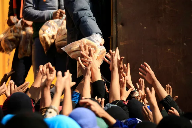 Displaced Iraqi people who fled from homes during a battle between Iraqi forces and Islamic State militants, receive bread at the Hammam al-Alil camp, south of Mosul, Iraq, March 14, 2017. (Photo by Thaier Al-Sudani/Reuters)