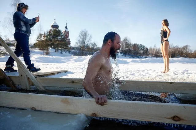 A woman poses for a picture near an ice hole as a man takes a dip during celebrations of the Orthodox Christian feast of Epiphany in the settlement of Ivanovskoye in the Moscow region, Russia on January 19, 2022. (Photo by Maxim Shemetov/Reuters)