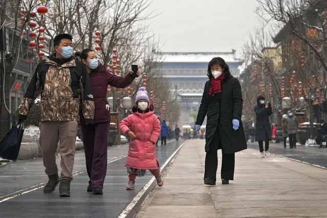 Family members wearing face masks to help protect from the coronavirus tour Qianmen Street, a popular tourist spot in Beijing, Sunday, January 23, 2022. (Photo by Andy Wong/AP Photo)