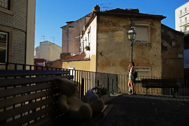 A woman stands by a street lamp as she takes photographs at Lisbon's Mouraria neighborhood, Portugal, Friday, July 10, 2015. The historical quarter, one of the oldest of the Portuguese capital, is a maze of narrow and cobble-stoned streets. (Photo by Francisco Seco/AP Photo)