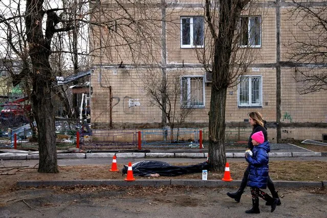 A woman and a child walk past a dead body in front of a residential building that was hit by a shell, as Russia's attack on Ukraine continues, in the Obolon district in Kyiv, Ukraine, March 14, 2022. (Photo by Thomas Peter/Reuters)