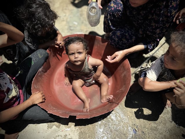 A Palestinian woman bathes a baby to cool him off as Palestinians struggle with increasing temperatures in the makeshift tents they take shelter in after Israeli attacks destroy their homes in Deir al Balah, Gaza on June 27, 2024. (Photo by Doaa Albaz/Anadolu via Getty Images)