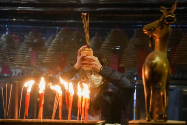 A worshipper wearing a face mask makes offerings of incense sticks on Lunar New Year's Eve, at the Man Mo Temple in Hong Kong, China, January 31, 2022. (Photo by Lam Yik/Reuters)