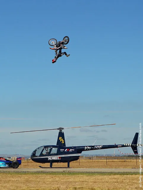 Australian Motorcross rider and member of the Crusty Demons, Robbie Marshall jumps over a helicopter with rotating blades and a Formula 1 car at Avalon Airport