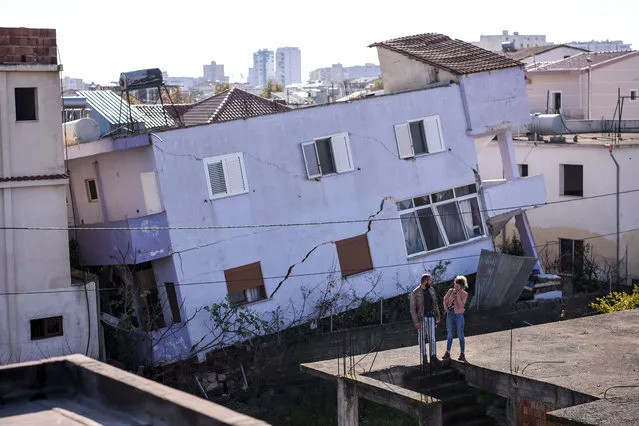 People stand in front of a collapsed building in the town of Durres, western Albania on November 27, 2019, after an earthquake hit Albania. Albania was in national mourning on November 27 as emergency workers continued to pull bodies from the ruins of buildings gutted by a violent earthquake, with nearly 30 dead found so far and more than 40 rescued alive. Tirana declared a state of emergency in the areas hardest-hit by the November 26 pre-dawn earthquake: the coastal city of Durres and the town of Thumane, where victims were trapped by toppled buildings. (Photo by Armend Nimani/AFP Photo)