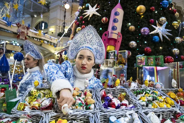 A seller dressed as Snegurochka (The Snow Maiden) shows Christmas toys at the Christmas decorations set in the Moscow GUM State Department store in Moscow, Russia in Moscow, Russia, Monday, December 16, 2019. (Photo by Pavel Golovkin/AP Photo)