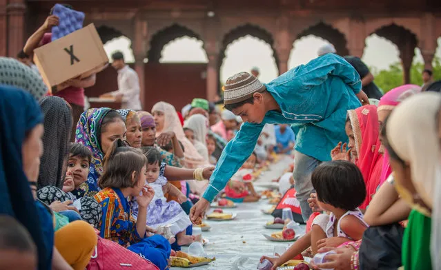 A boy distributes fruit to women at a mosque during Iftar, the evening meal when Muslims end their daily Ramadan fast at sunset in Delhi, India on June 7, 2016. (Photo by Shams Qari/Barcroft Images)