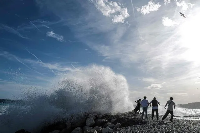 People stand in front of big waves on the “Promenade des anglais” in the French riviera city of Nice, on April 8, 2022. (Photo by Valery Hache/AFP Photo)
