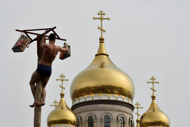 A man climbs up a wooden pole to get a prize in front of an Orthodox cathedral during celebrations of Maslenitsa, also known as Pancake Week, which is a pagan holiday marking the end of winter, in Vladivostok, Russia on March 1, 2020. (Photo by Yuri Maltsev/Reuters)