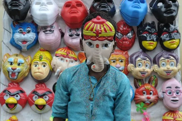 An Indian boy wears a mask of Hindu deity Ganesh sell outside a temple during the “Ganesh Chaturthi” festival in Hyderabad on August 25, 2017. The Ganesh Chaturthi festival, a popular 11-day religious festival which is annually celebrated across India, runs this year from August 25 to September 5. During the festival devout Hindus pray to idols of Lord Ganesha at their homes and temporary makeshift temple, culminating with the immersion of the idols in the Bay of Bengal. (Photo by Noah Seelam/AFP Photo)