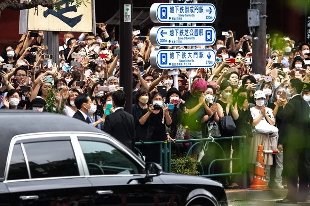 People watch the hearse transporting the body of late former Japanese prime minister Shinzo Abe as it leaves Zojoji Temple in Tokyo on July 12, 2022. (Photo by Philip Fong/AFP Photo)