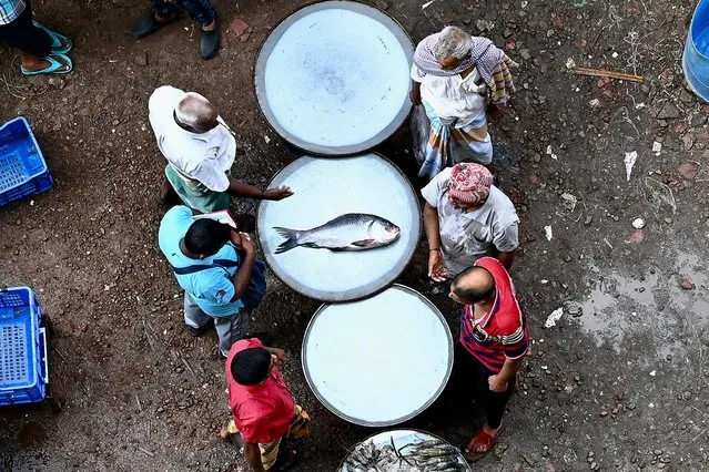 People look at a fish on display for sale at fish market next to the Buriganga River in Dhaka on July 21, 2022. (Photo by Munir Uz Zaman/AFP Photo)
