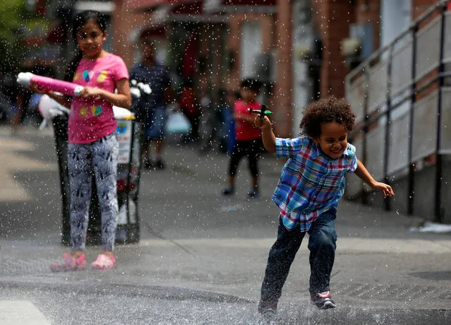 Children run through water spraying from a fire hydrant in the Queens borough of New York, U.S., July 6, 2016. (Photo by Shannon Stapleton/Reuters)