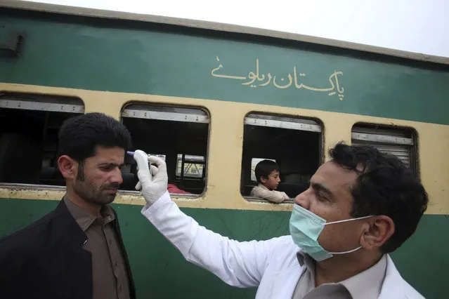 A Pakistani volunteer checks the body temperature of passengers arriving at a railway station in Peshawar, Pakistan, Tuesday, March 17, 2020. For most people, the new coronavirus causes only mild or moderate symptoms. For some it can cause more severe illness. (Photo by Muhammad Sajjad/AP Photo)