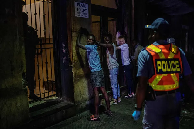 Suspects are lined up against a wall as a member of the South African Police Service (SAPS) wearing gloves arrests them because they defied the lockdown order during an operation in the Johannesburg CBD, on March 27, 2020. South Africa came under a nationwide military-patrolled lockdown on March 27, 2020, joining other African countries imposing strict curfews and shutdowns in an attempt to halt the spread of the COVID-19 coronavirus across the continent. (Photo by Michele Spatari/AFP Photo)