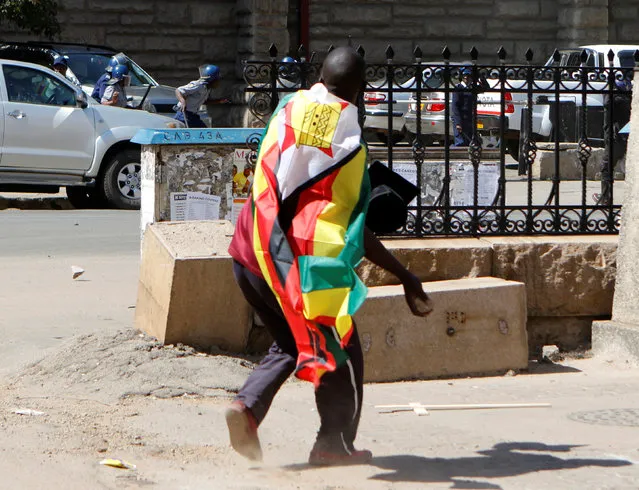 A man with a Zimbabwean flag wrapped around him throws stones at police officers during a protest against President Robert Mugabe's government's handling of the economy in Harare, Zimbabwe August 3, 2016. (Photo by Philimon Bulawayo/Reuters)