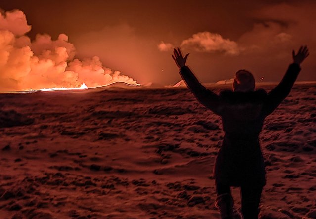 A local resident watch smoke billow as the lava colour the night sky orange from an volcanic eruption on the Reykjanes peninsula 3 km north of Grindavik, western Iceland on December 18, 2023. A volcanic eruption began on Monday night in Iceland, south of the capital Reykjavik, following an earthquake swarm, Iceland's Meteorological Office reported. (Photo by Kristin Elisabet Gunnarsdottir/AFP Photo)