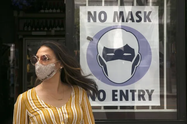 A woman walks out of a liquor store past a sign requesting its customers to wear a mask Tuesday, June 23, 2020, in Santa Monica, Calif. The state Department of Public Health recorded more than 5,000 new cases Tuesday, putting the total number of positive cases at more than 183,000. The state has seen more than 5,500 deaths related to COVID-19. (Photo by Jae C. Hong/AP Photo)