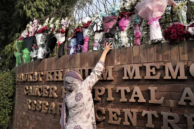 A woman places bouquet over the wall of a hospital where former Pakistani Prime Minister Imran Khan is being treated for a gunshot wound in Lahore, Pakistan, Friday, November 4, 2022. Khan who narrowly escaped an assassination attempt on his life the previous day when a gunman fired multiple shots and wounded him in the leg, is listed in stable condition after undergoing surgery at a hospital, a senior leader from his party said Friday. (Photo by K.M. Chaudhry/AP Photo)