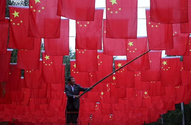 A man hangs Chinese national flags as decorations at a park, ahead of China's National Day, in Beijing September 29, 2015. (Photo by Reuters/China Daily)