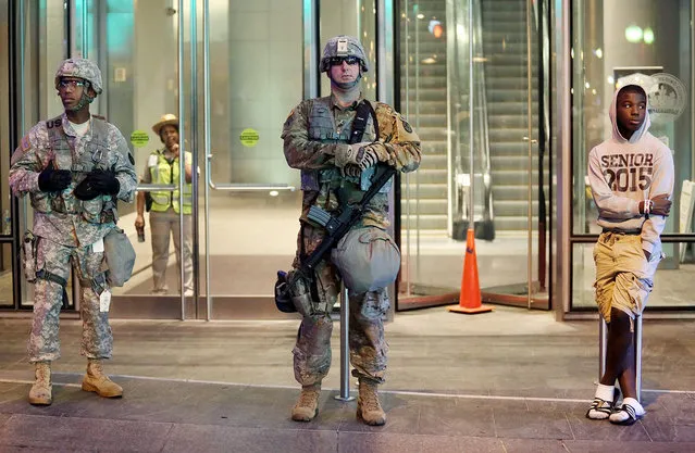 An adolescent boy (R) stands next to members of the North Carolina National Guard guarding an office building in downtown Charlotte, North Carolina, USA, 22 September 2016. North Carolina governor Pat McCrory declared a state of emergency after protesters took to the streets of Charlotte, North Carolina, for the second night in a row, demonstrating against the fatal shooting of African-American Keith Lamont Scott by police officers. (Photo by Veasey Conway/EPA)