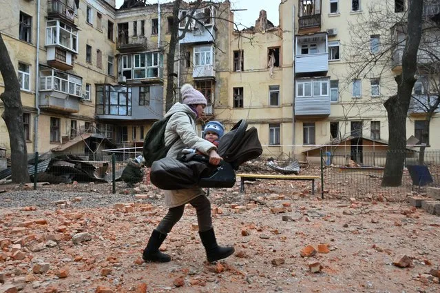 A local resident carries her baby outside of their residential building partially destroyed after a missile strike in Kharkiv on January 30, 2023, amid the Russian invasion of Ukraine. (Photo by Sergey Bobok/AFP Photo)