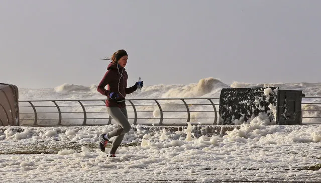A woman jogs through sea foam in Blackpool northwest England as a storm lashed Britain with violent storm-force winds of up to 100mph, leaving thousands of homes without power and hitting transport links Wednesday January 3, 2018. (Photo by Peter Byrne/PA Wire via AP Photo)