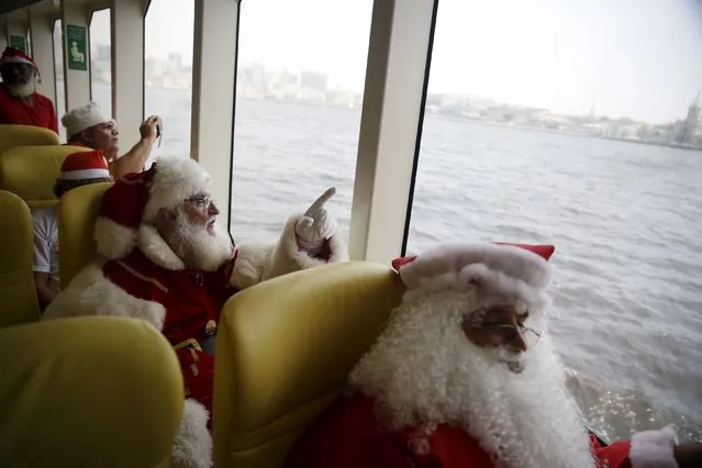 Students of the "Escola de Papai Noel do Brasil" (Brazil's school of Santa Claus) look from a ferry as they travel through Guanabara bay, during their graduation ceremony in Rio de Janeiro, Brazil, November 10, 2015. The school holds 4 days' lessons in Santa-training, teaching Christmas carols, how to interact with children, and also how to wear the heavy red suit in Rio's typical 104-degree (40 degrees celsius) summer weather that is common around the holidays. (Photo by Pilar Olivares/Reuters)