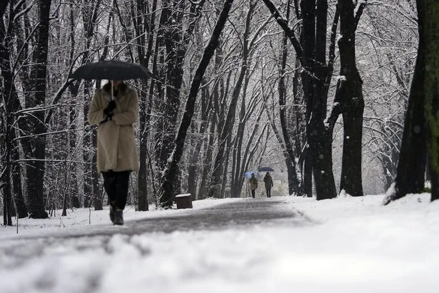 A woman walks through a snow covered park in Belgrade, Serbia, Sunday, February 26, 2023. Serbia and the rest of the region were hit by a sudden weather change this weekend that brought rain and snow after a warm period. (Photo by Darko Vojinovic/AP Photo)