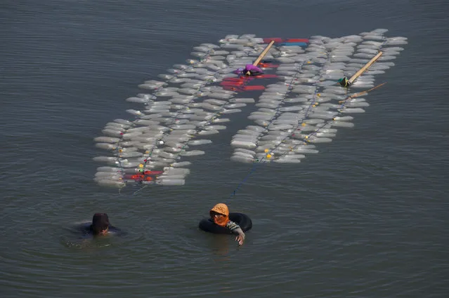 This photo taken on March 21, 2018 shows Indonesian Murni (L) with her fellow villager swimming back to their village with jars of clean water in Tinambung, West Sulawesi. Indonesian villager Mama Hasria swims upstream with about 200 empty jerry cans tied to her back, a daily trip she and other local women make to get clean water for their community on Sulawesi island. As a scorching sun beats down, the 46-year-old Hasria makes the four kilometre (2.5 mile), hour-long trip along the murky. (Photo by Yusuf Wahil/AFP Photo)