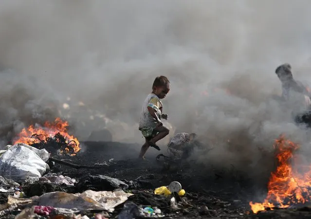 A Filipino boy runs amid black smoke billowing from electrical wires being burned by scavengers at a dumpsite in Manila, Philippines on Thursday, January 8, 2015. (Photo by Aaron Favila/AP Photo)