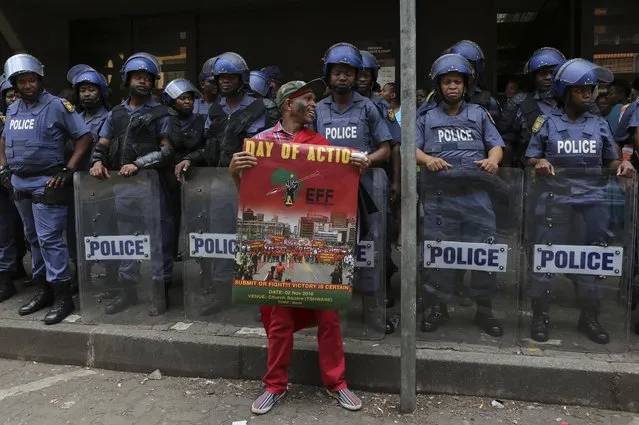 Riot police guard the entrance to a courthouse in Pretoria, South Africa, Wednesday, November 2, 2016, as an Economic Freedom Fighters supporter protests. Thousands of South Africans are demonstrating for the resignation of President Jacob Zuma, who has been enmeshed in scandals that critics say are undermining the country's democracy. (Photo by Denis Farrell/AP Photo)