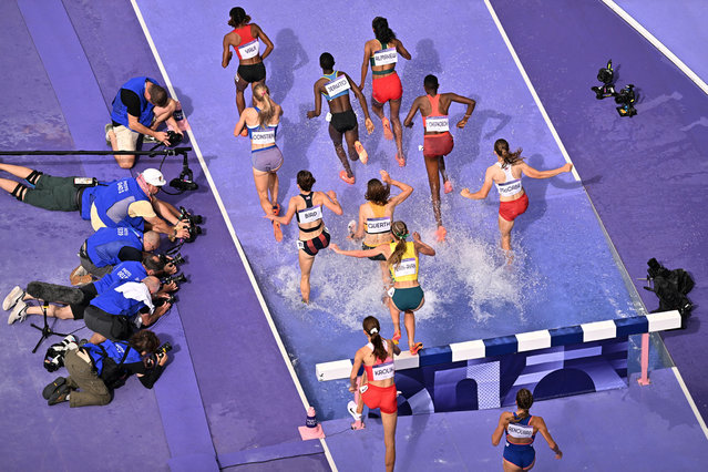 An overview shows athletes competing as photographers take picture during the women's 3000m steeplechase heat of the athletics event at the Paris 2024 Olympic Games at Stade de France in Saint-Denis, north of Paris, on August 4, 2024. (Photo by Antonin Thuillier/AFP Photo)
