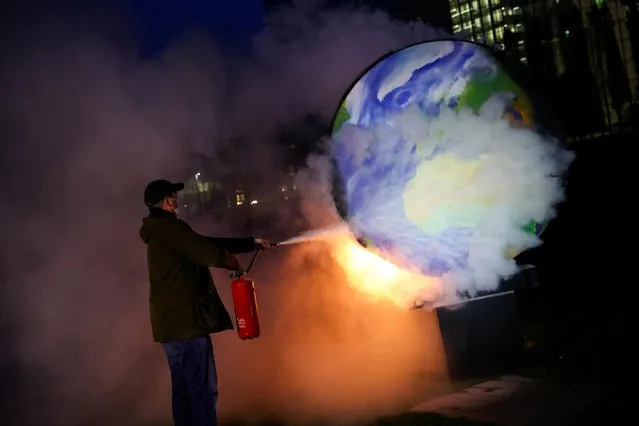 A person uses an extinguisher on a burning paper-made globe during a demonstration against the fossil fuel industry, in front of the headquarters of the European Central Bank (ECB) in Frankfurt, Germany, October 21, 2020. (Photo by Kai Pfaffenbach/Reuters)