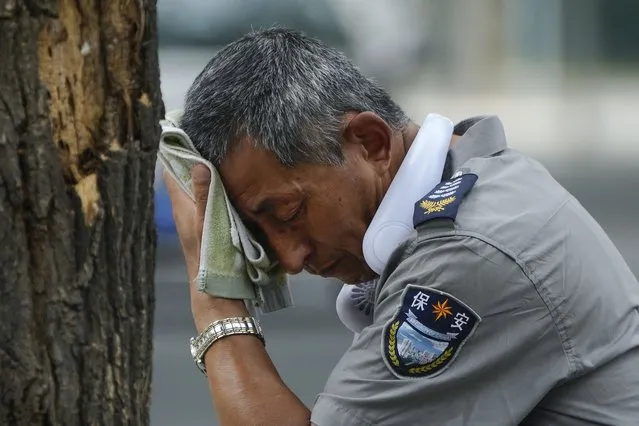 A security guard wearing an electric fan on his neck wipes his sweat on a hot day in Beijing, Monday, July 3, 2023. Heavy flooding has displaced thousands of people around China as the capital had a brief respite from sweltering heat. Beijing reported 9.8 straight days when the temperature exceeded 35 C (95 F), the National Climate Center said Monday. (Photo by Andy Wong/AP Photo)