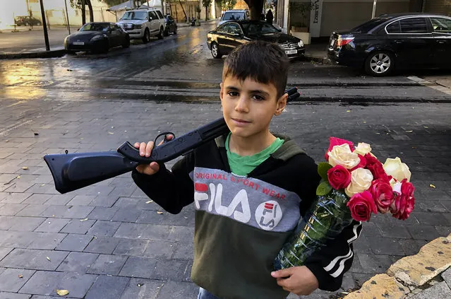 A displaced Syrian boy, Omar, 10, who sells flowers on the street and who fled the war from his hometown of Hassakeh, holds a toy gun and flowers in Hamra street, Beirut, Lebanon, January 31, 2021. UNICEF said Wednesday, March 10, 2021 that Syria’s 10-year-long civil war has killed or wounded about 12,000 children and left millions out of school in what could have repercussions for years to come in the country. The country's bitter conflict has killed nearly half a million people, wounded more than a million and displaced half the country’s population, including more than 5 million as refugees. (Photo by Hussein Malla/AP Photo)