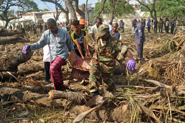 People carry the body of a victim at the scene of a car bomb attack near the port of the capital Mogadishu, on December 11, 2016. More than 20 people were killed on December 11 in a suicide truck bombing in the Somali capital Mogadishu, police said, in a fresh strike claimed by the Al-Qaeda-linked Shabaab group. (Photo by Mohamed Abdiwahab/AFP Photo)