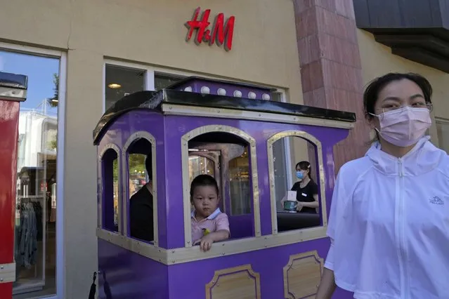 A child in a toy train passes a H&M store in Beijing on Thursday, June 3, 2021. The Chinese government has accused H&M, Nike, Zara and other brands of importing unsafe or poor quality children's clothes and other goods, adding to headaches for foreign companies after Beijing attacked them over complaints about possible forced labor in the country's northwest. (Photo by Ng Han Guan/AP Photo)