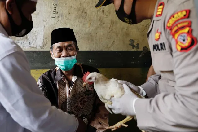 Lili Dinata, 72-year-old local of Sindanglaya village, is being rewarded with a live chicken by Galih Apria, the district police chief, after receiving his first dose of a COVID-19 vaccine, during a door-to-door vaccination in Cianjur regency, West Java province, Indonesia, June 15, 2021. (Photo by Willy Kurniawan/Reuters)