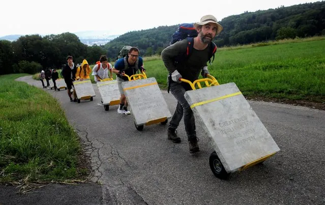The Swiss concept artists Frank (R) and Patrik Riklin along with volunteers push ten sandstone slabs called 10 Commandments Vol. 2, each weighing 100 kilograms, on trolleys up a road near Spreitenbach, Switzerland on June 29, 2021. (Photo by Arnd Wiegmann/Reuters)