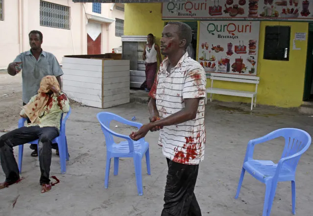 A Somali man helps a wounded civilian while another one waits for help after a car bomb was detonated at the gate of one of Mogadishu's most popular hotel, Friday, March, 27, 2015. A Somali police official says a suicide bomber has detonated his explosives-laden car at the gate of a hotel popular with government officials in Mogadishu. (Photo by Farah Abdi Warsameh/AP Photo)