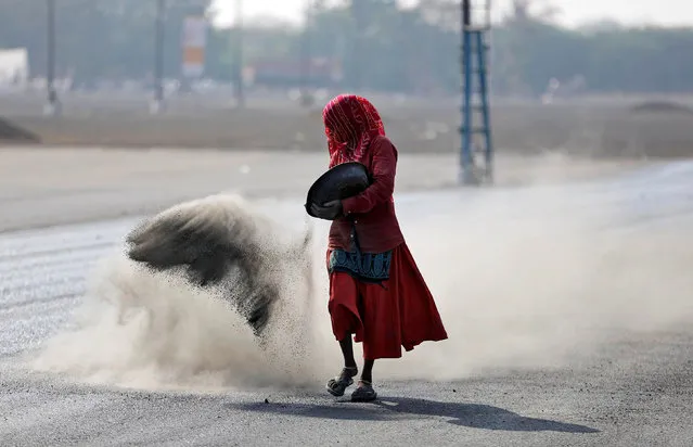 A woman throws a mixture of black ash, cement, concrete powder and ordinary dust over newly constructed road tarmac to dry it and fill in the gaps, in Ahmedabad, India January 6, 2017. (Photo by Amit Dave/Reuters)