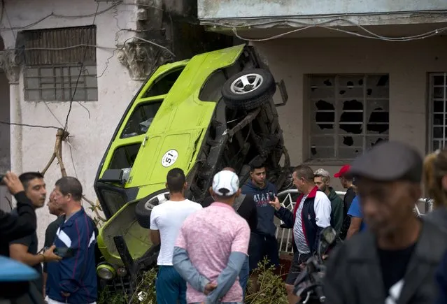 People stand around a car that was overturned by a tornado in Havana, Cuba, Monday, January 28, 2019. A tornado and pounding rains smashed into the eastern part of Cuba's capital overnight, toppling trees, bending power poles and flinging shards of metal roofing through the air as the storm cut a path of destruction across eastern Habana. (Photo by Ramon Espinosa/AP Photo)