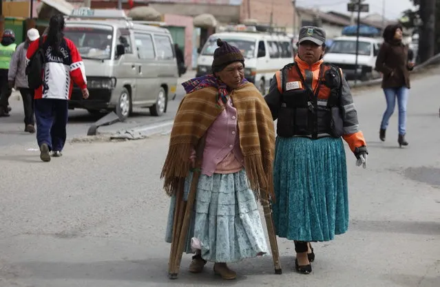 In this December 13, 2013 photo, an Aymara traffic policewomen, right, aids a woman in crossing a street in El Alto, Bolivia. (Photo by Juan Karita/AP Photo)