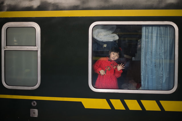 A girl waves from inside a train as she and her family (not seen) prepare to depart for their hometown for the “Spring Festival” or Lunar New Year on January 24, 2017 at Beijing Railway Station The huge movement of Chinese travelling home to spend the Lunar New Year with their families is often described as the world' s largest human migration and overcrowded planes, trains and automobiles are the norm. (Photo by Nicolas Asfouri/AFP Photo)