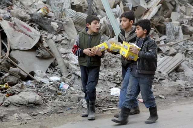 Boys carry boxes of biscuits near rubble of damaged buildings in Aleppo, Syria March 2, 2016. (Photo by Abdalrhman Ismail/Reuters)